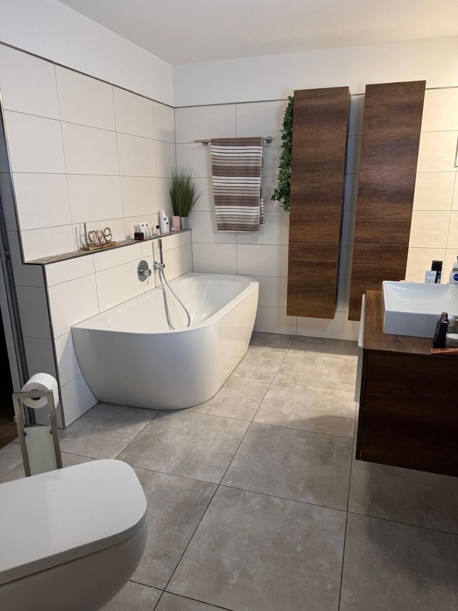 Fertiges Badezimmer mit freistehender Wanne, großen grauen Bodenfliesen und Waschtisch in dunklem Holz
